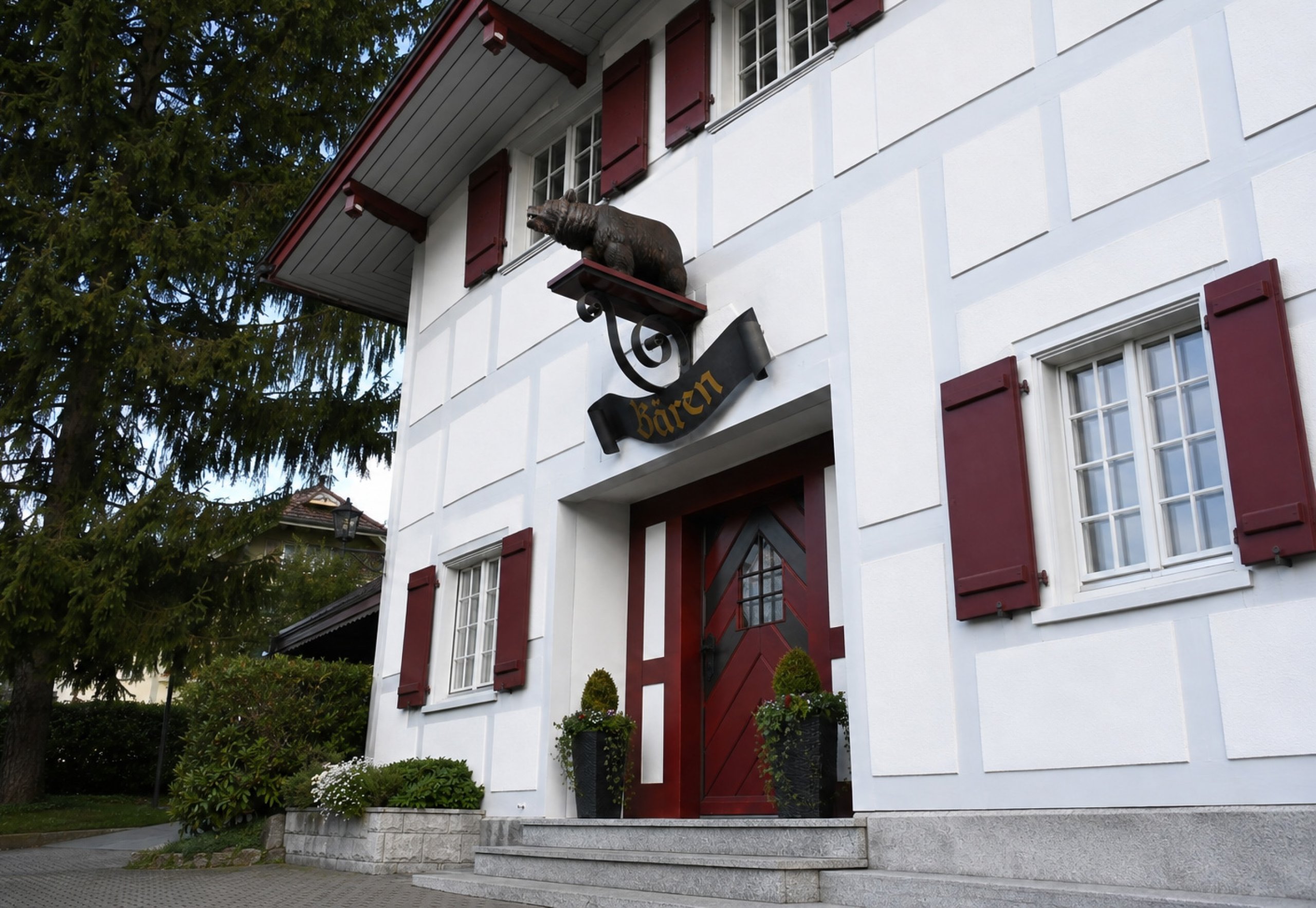 Aussenansicht des Gasthofs Bären Gerzensee mit weiss-grauer Fassade und bordeauxroten Fensterläden